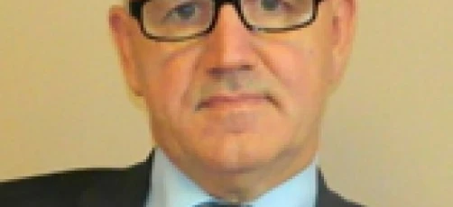 A close-up image of a person wearing glasses and a formal collar. Their chin, eyebrow and forehead are visible, along with their jaw and neck.