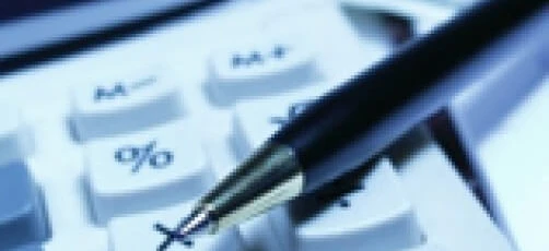 A calculator and a pen on a desk with paper and office supplies. The image shows office equipment and electronic devices used in an office setting.