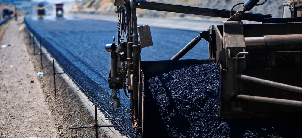 Ciężki sprzęt rozładowuje asfalt na powierzchni drogi, tworząc gładką autostradę. Maszyna układa smołę, beton i żwir, niezbędne materiały budowlane do projektów infrastrukturalnych.